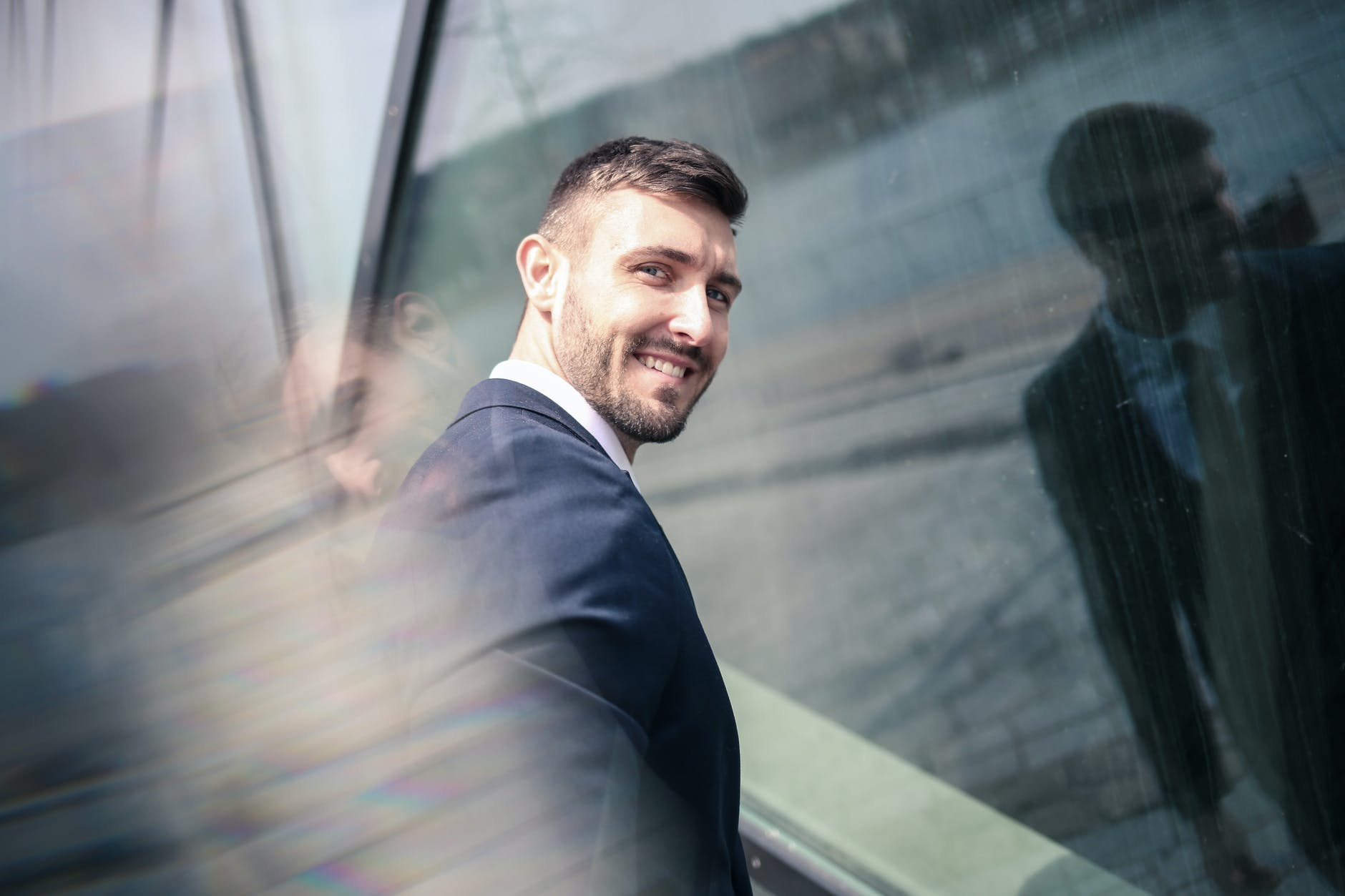 cheerful businessman in formal wear standing in front of glass wall