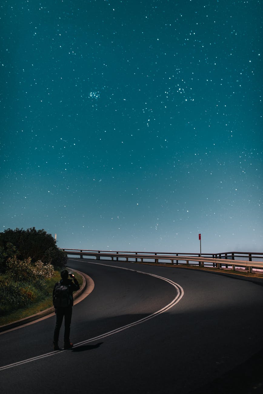 anonymous tourist taking photo of starry sky while standing on road