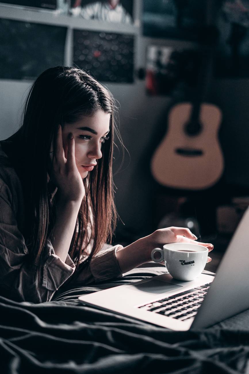 photo of woman lying on bed while using laptop